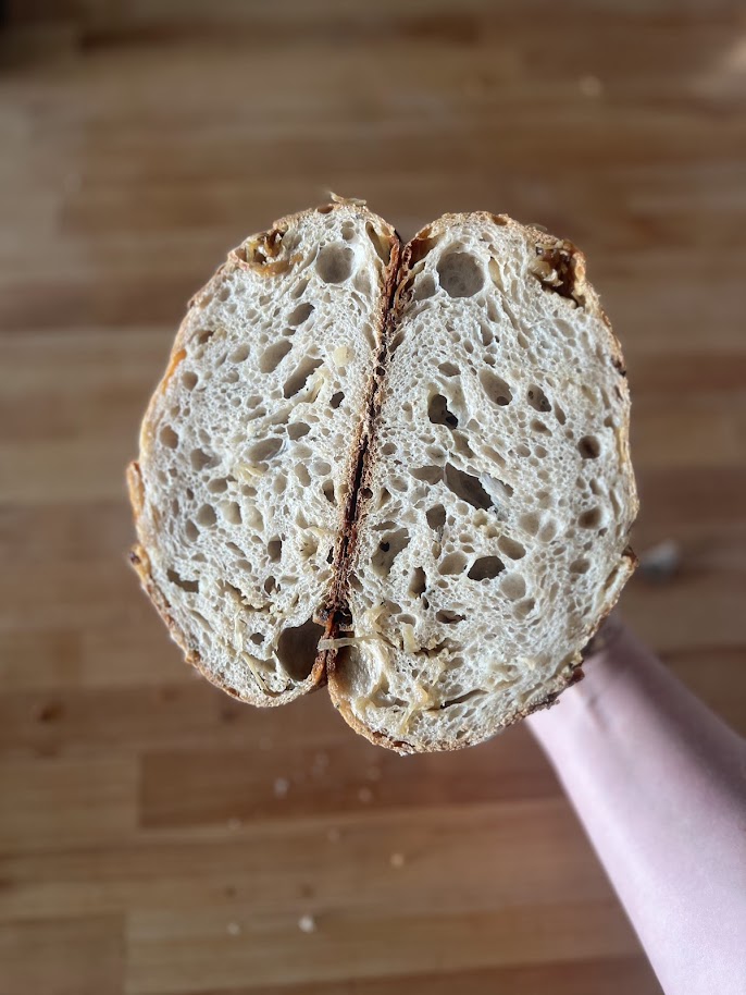 A sliced french onion sourdough loaf held up to show an open, even crumb ribboned with caramelized onion