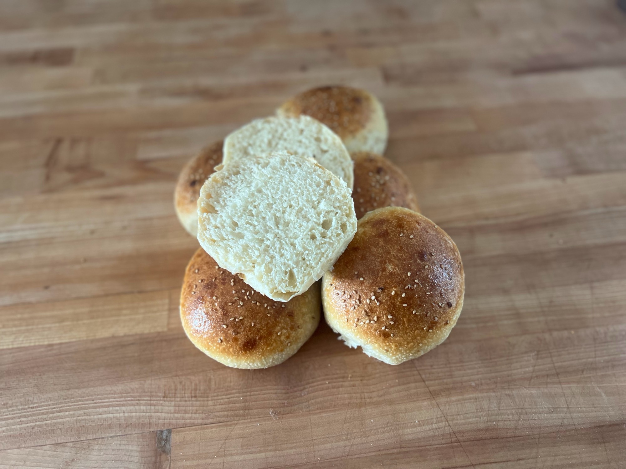 An onion burger bun sliced open to show a soft, even, pale-gold crumb, resting on a pile of sesame-topped buns