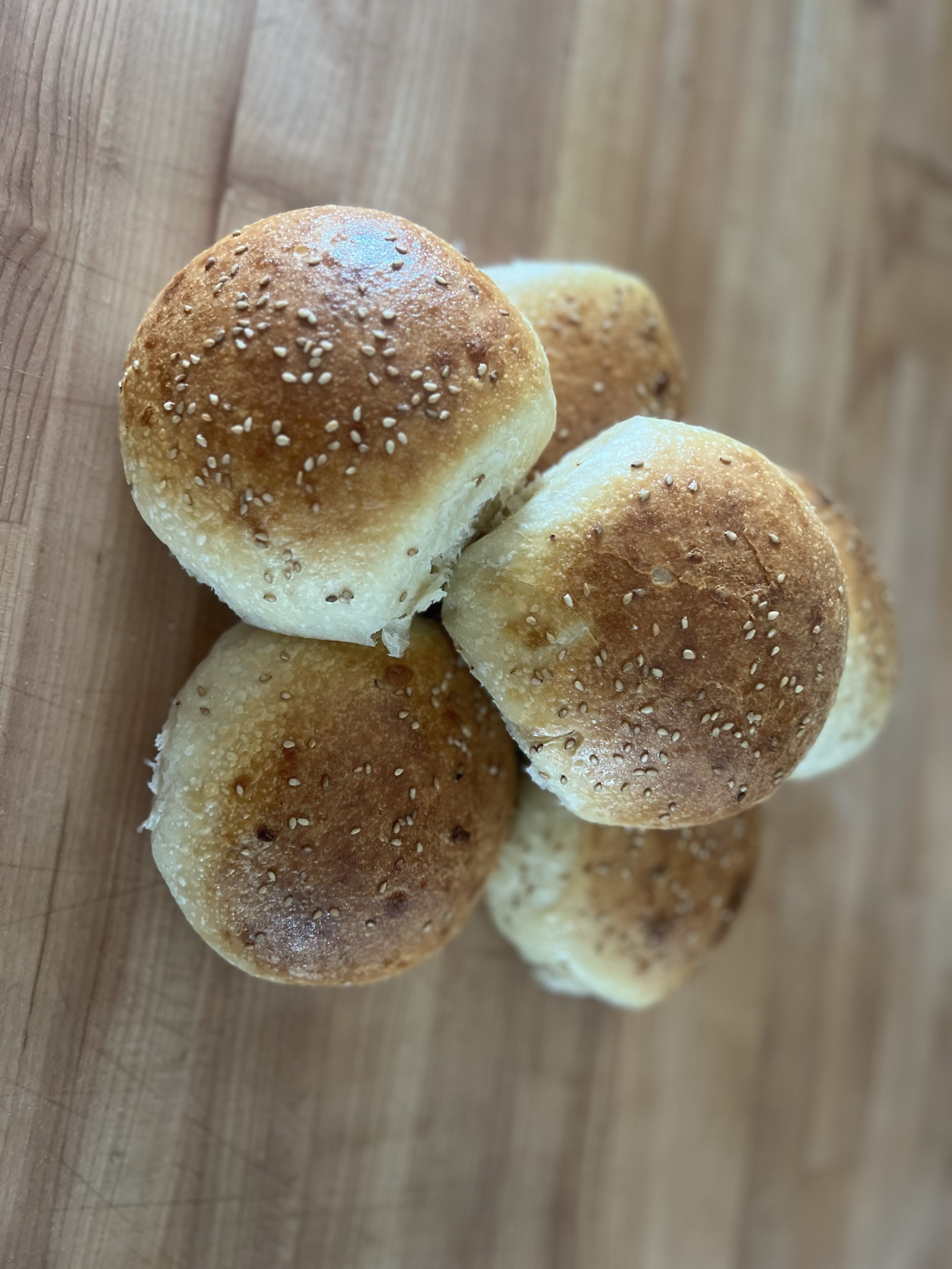 A stack of glossy golden-brown sesame-topped onion burger buns on a wooden butcher block