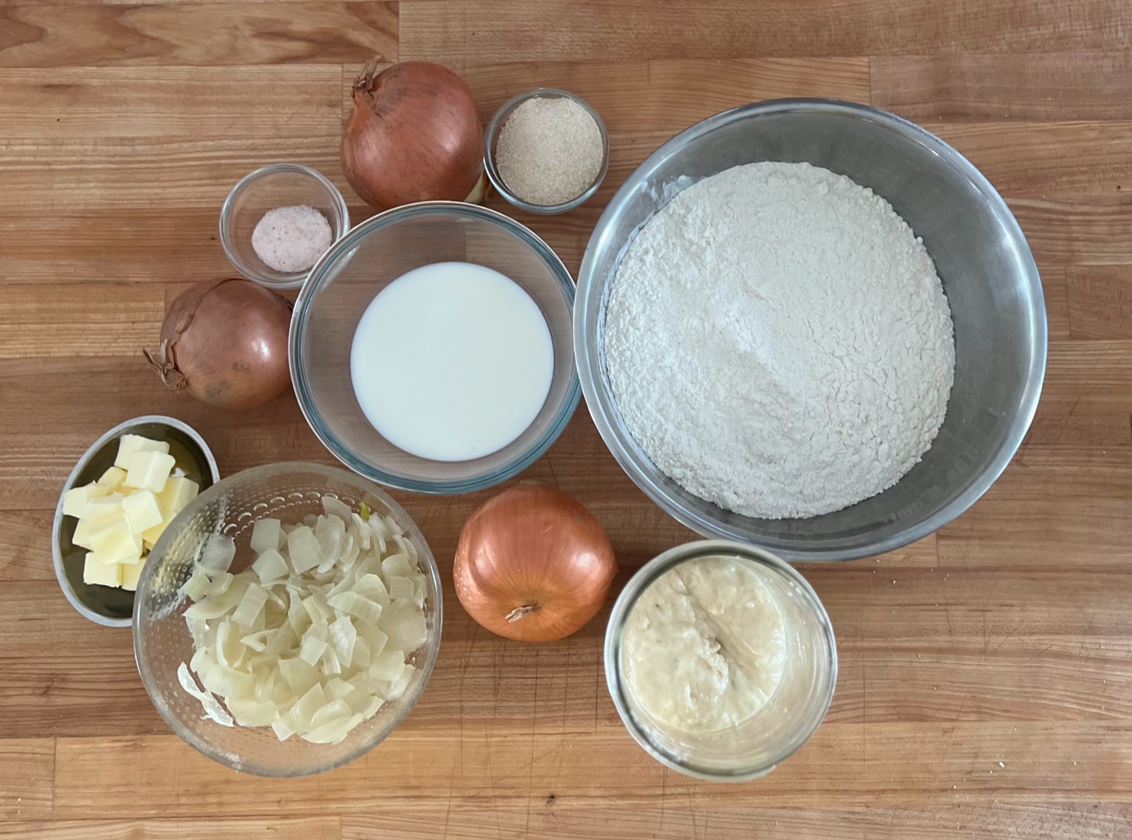 Laila's wooden work bench laid out with flour, milk, butter, onions, and a jar of sourdough starter, ready for a bake